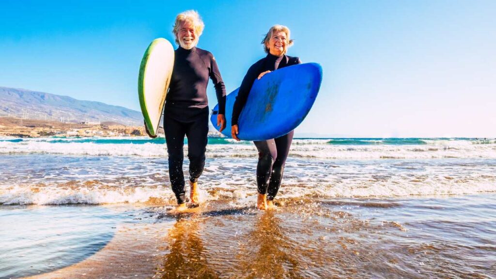 Retired couple walking on the beach with surf boards